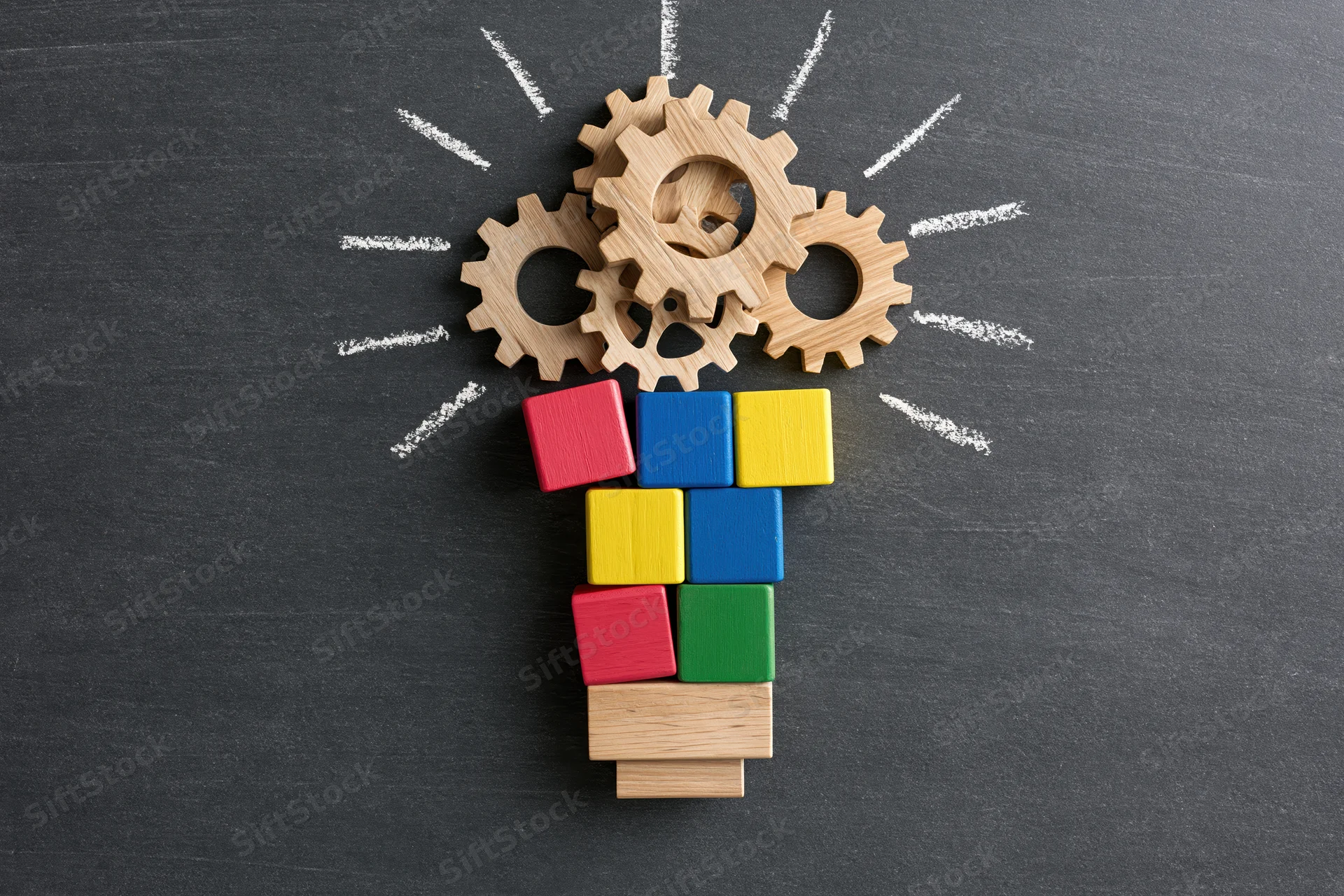 Wooden gears and colorful blocks arranged as a lightbulb on a blackboard