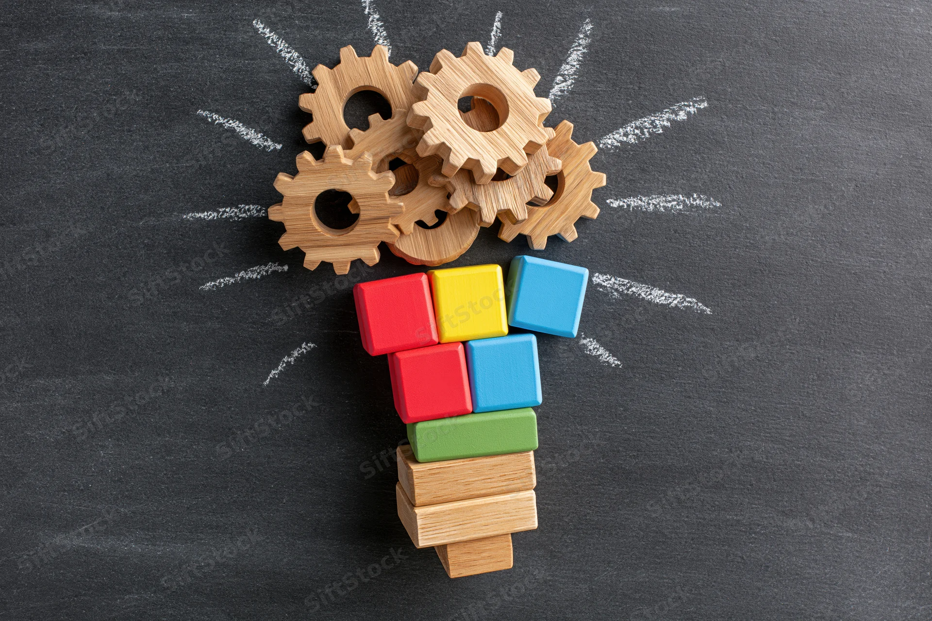 Wooden gears and colorful blocks arranged as a lightbulb on a chalkboard surface