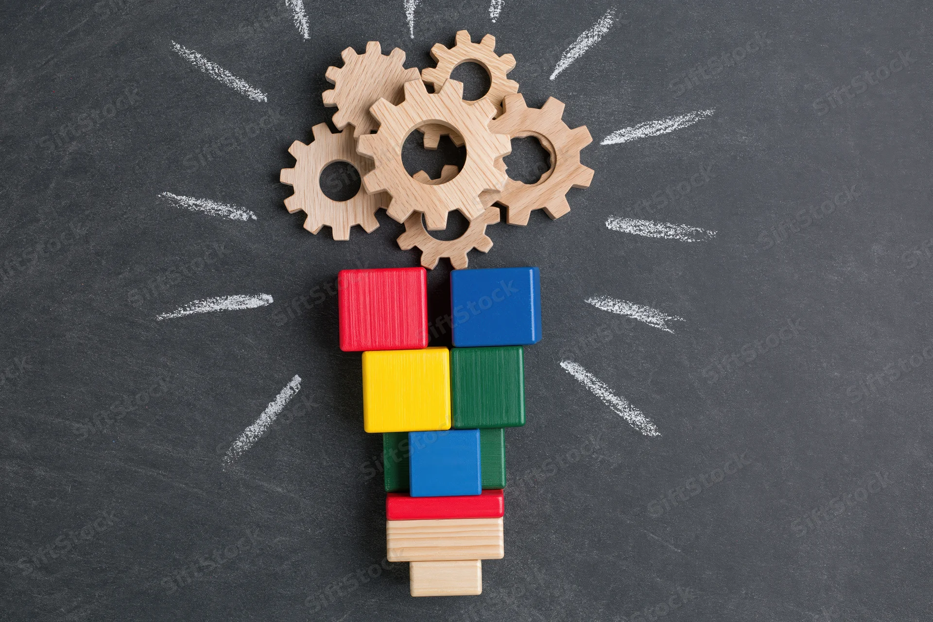 Wooden gears and colorful blocks arranged as a lightbulb on a chalkboard