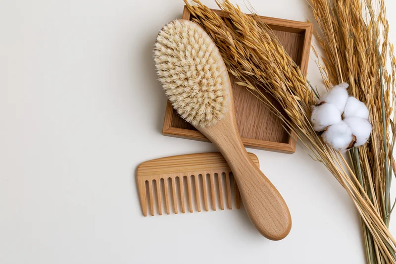 Wooden hairbrush and wide-tooth comb with wheat and cotton on white surface