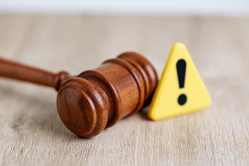 Wooden gavel lying beside a yellow warning triangle on a light wooden surface