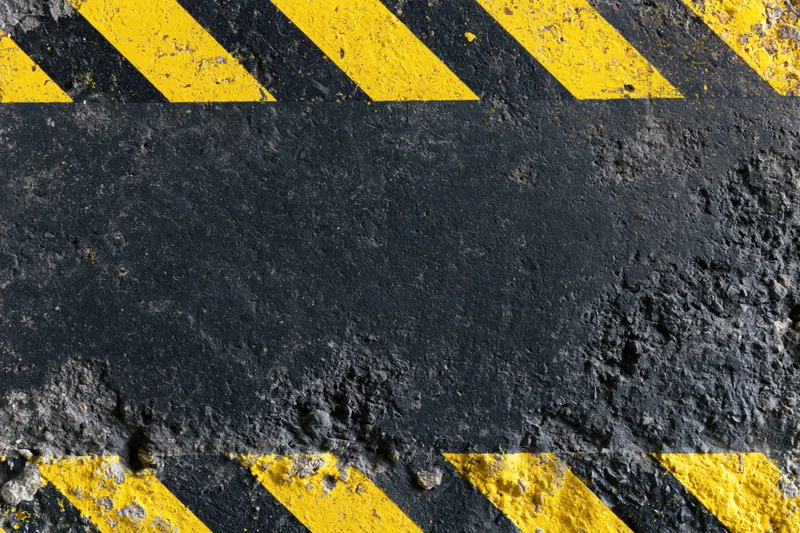 Worn industrial concrete surface with bold yellow and black diagonal hazard stripes