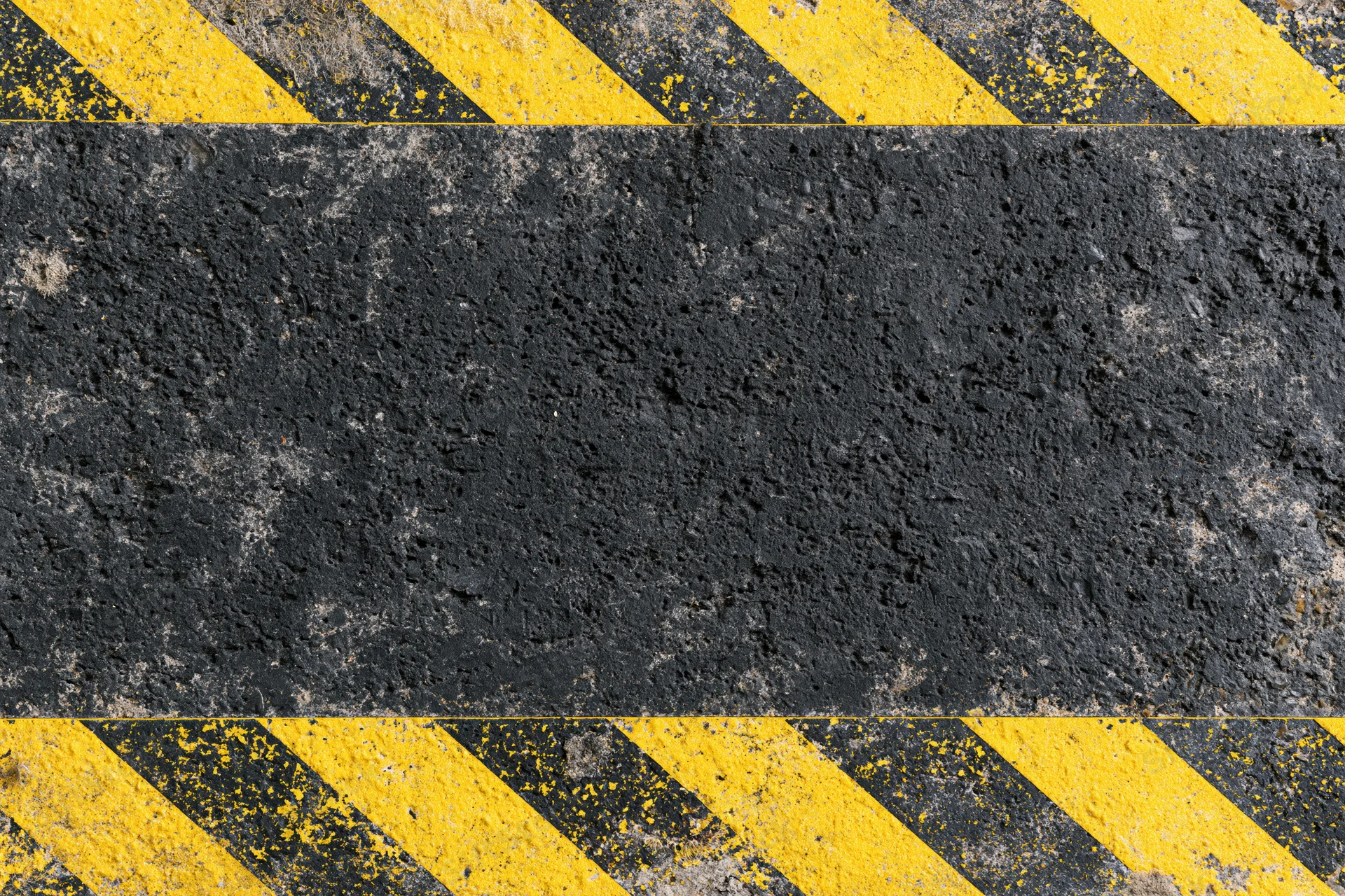 Worn industrial concrete surface with bold yellow and black diagonal hazard stripes