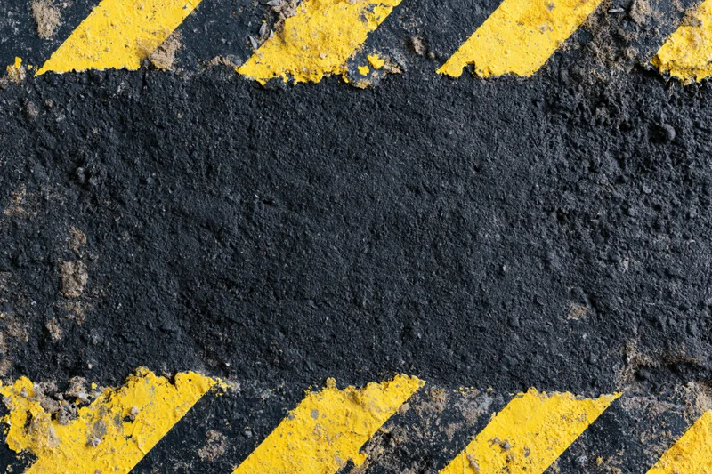 Worn industrial concrete surface with bold yellow and black diagonal hazard stripes