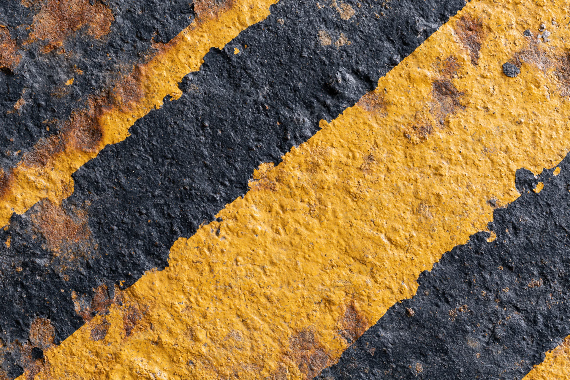 Diagonal yellow and black hazard stripes on a worn industrial metal surface with rust and peeling paint