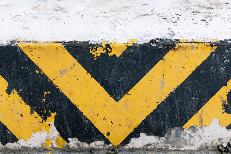 Weathered yellow and black chevron stripes on a concrete curb