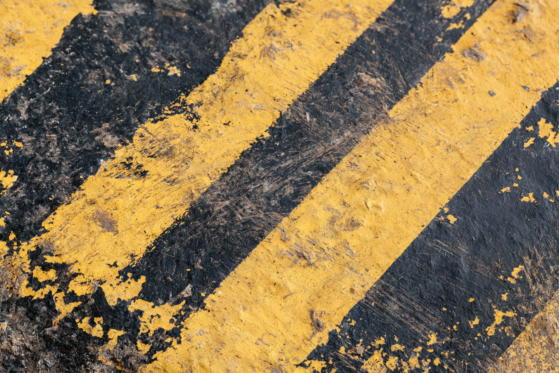 Worn yellow and black diagonal hazard stripes painted on asphalt pavement