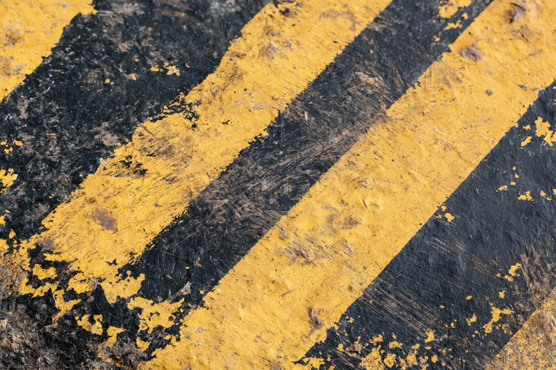 Worn yellow and black diagonal hazard stripes painted on asphalt pavement