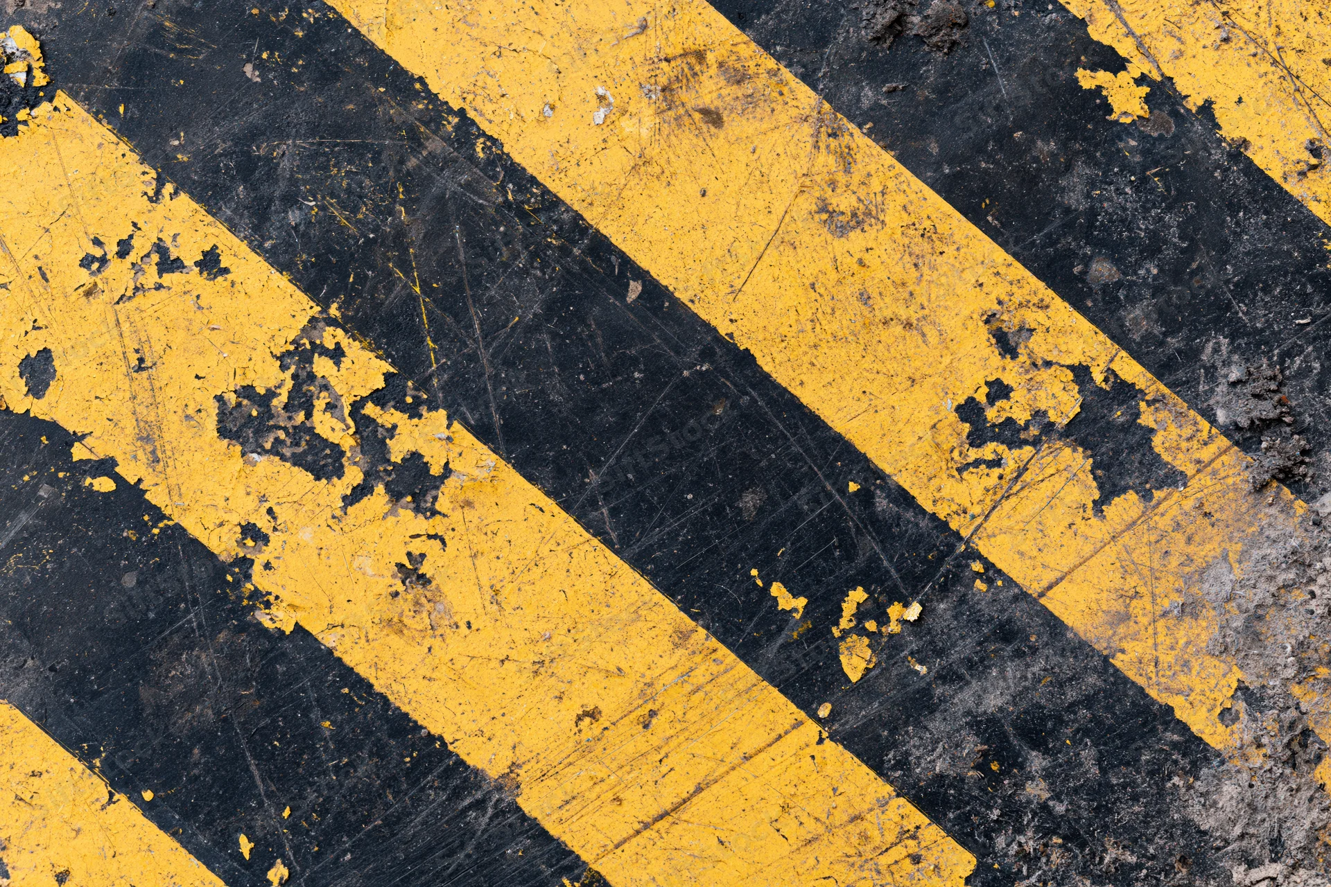 Worn yellow and black diagonal hazard stripes on asphalt pavement