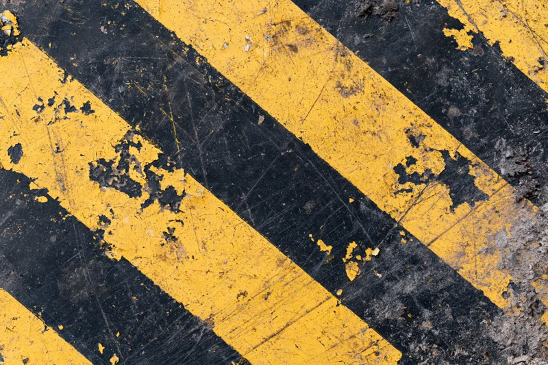Worn yellow and black diagonal hazard stripes on asphalt pavement