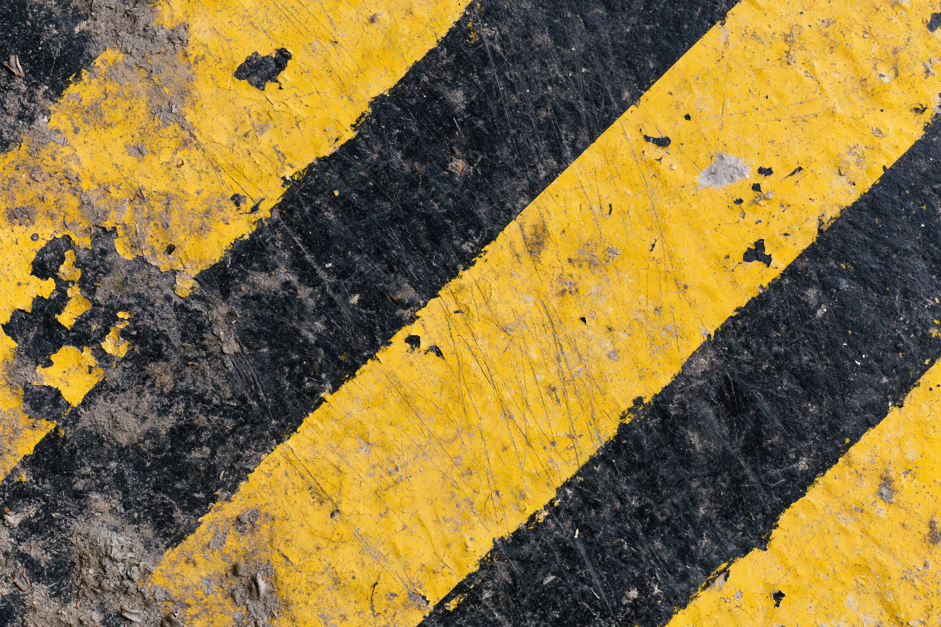 Worn yellow and black diagonal hazard stripes painted on asphalt pavement