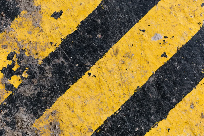 Worn yellow and black diagonal hazard stripes painted on asphalt pavement