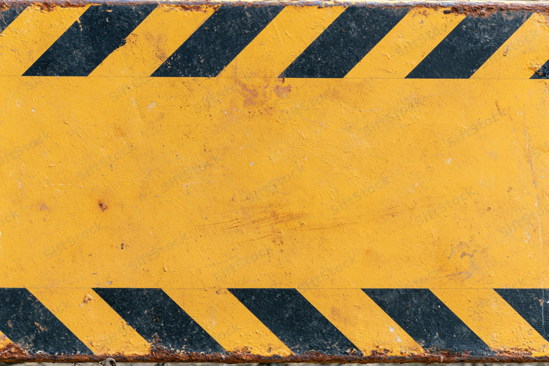 Worn yellow metal safety barrier panel with black diagonal hazard stripes