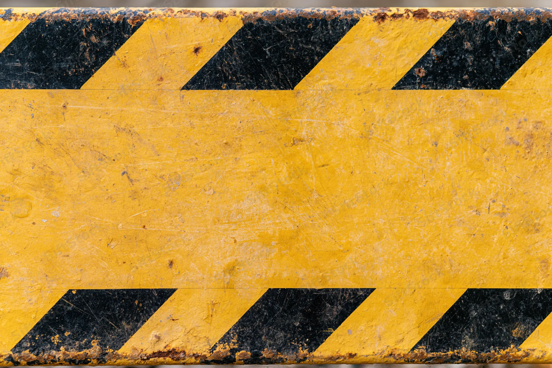 Worn yellow metal safety barrier panel with black diagonal stripes showing scratches and rust