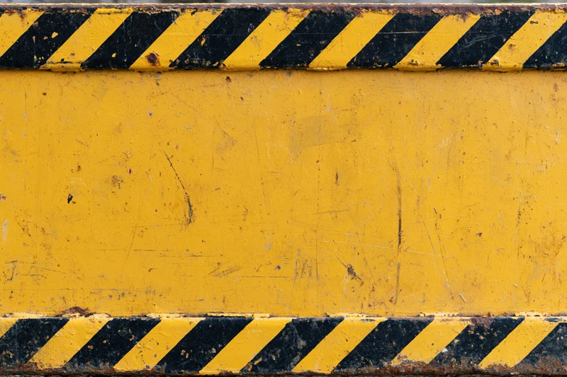 Worn yellow metal safety barrier panel with black diagonal hazard stripes