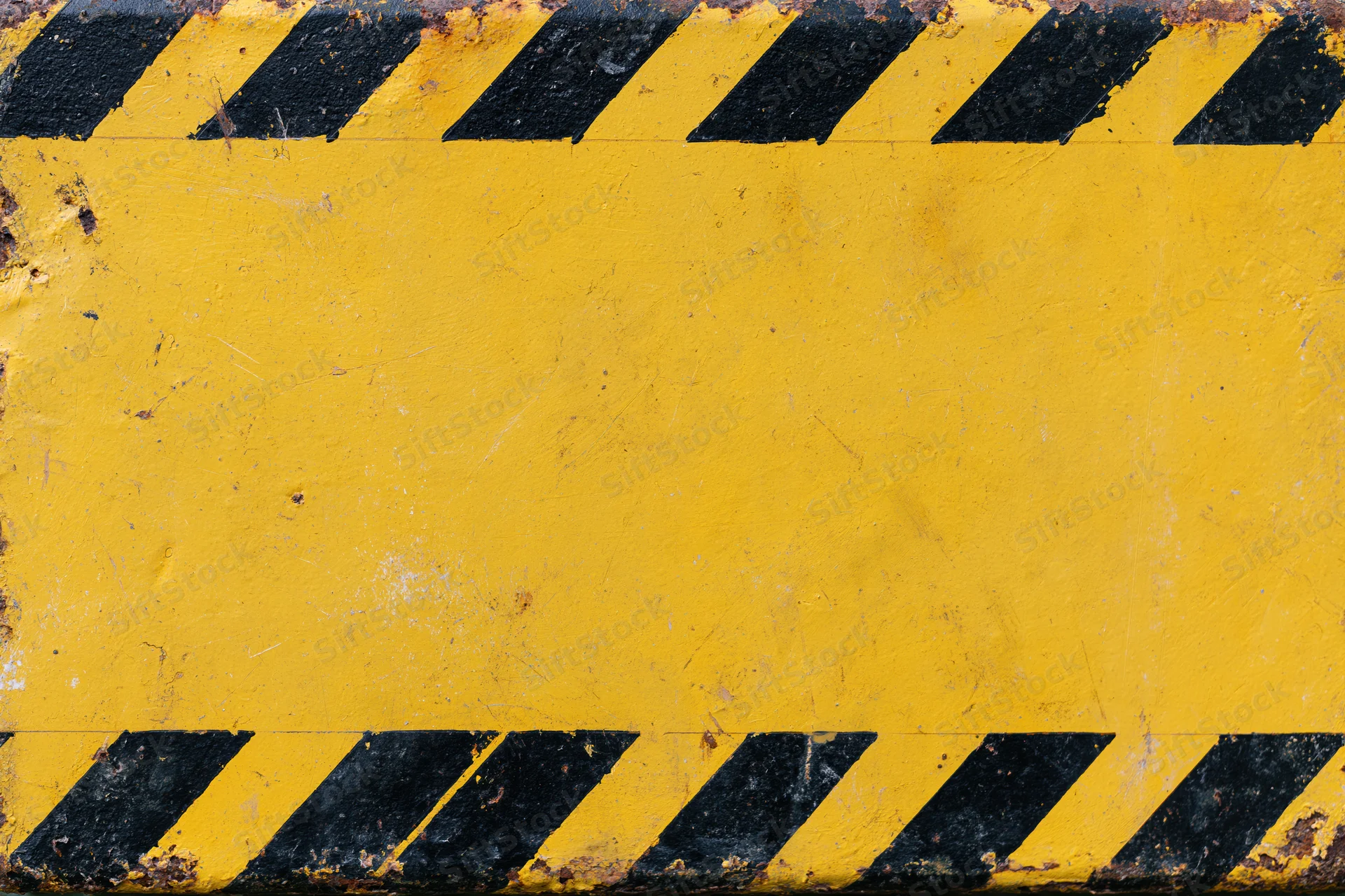 Worn yellow metal safety barrier panel with black diagonal hazard stripes