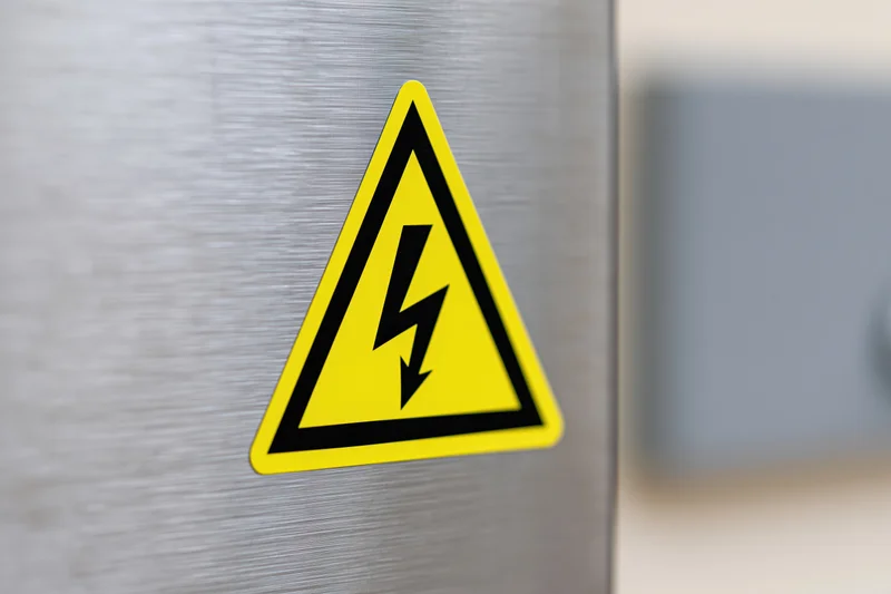 Yellow and black high voltage warning symbol on a brushed metal panel