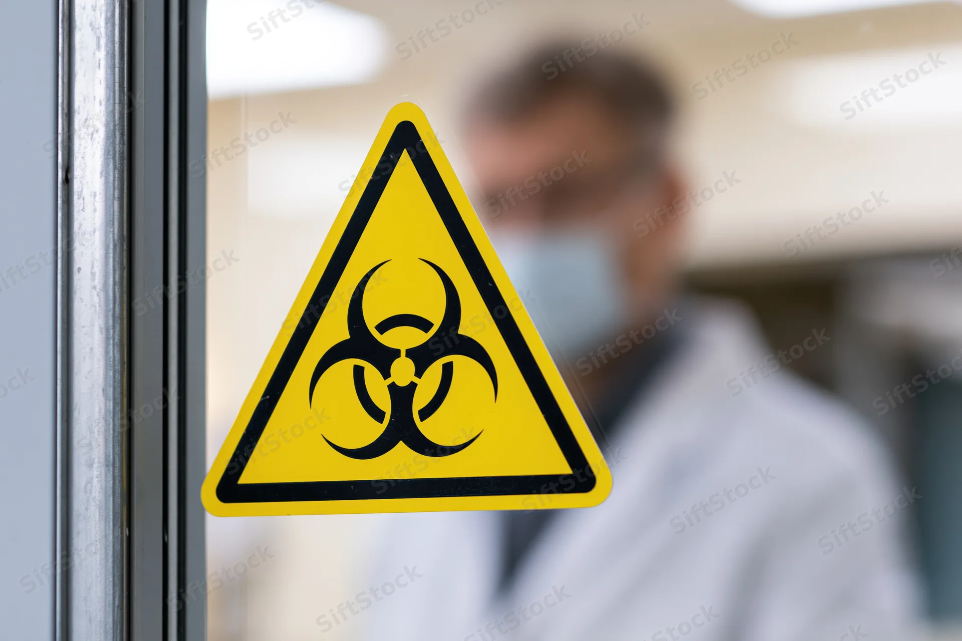 Biohazard warning sign on glass door with scientist in lab coat and mask blurred in background
