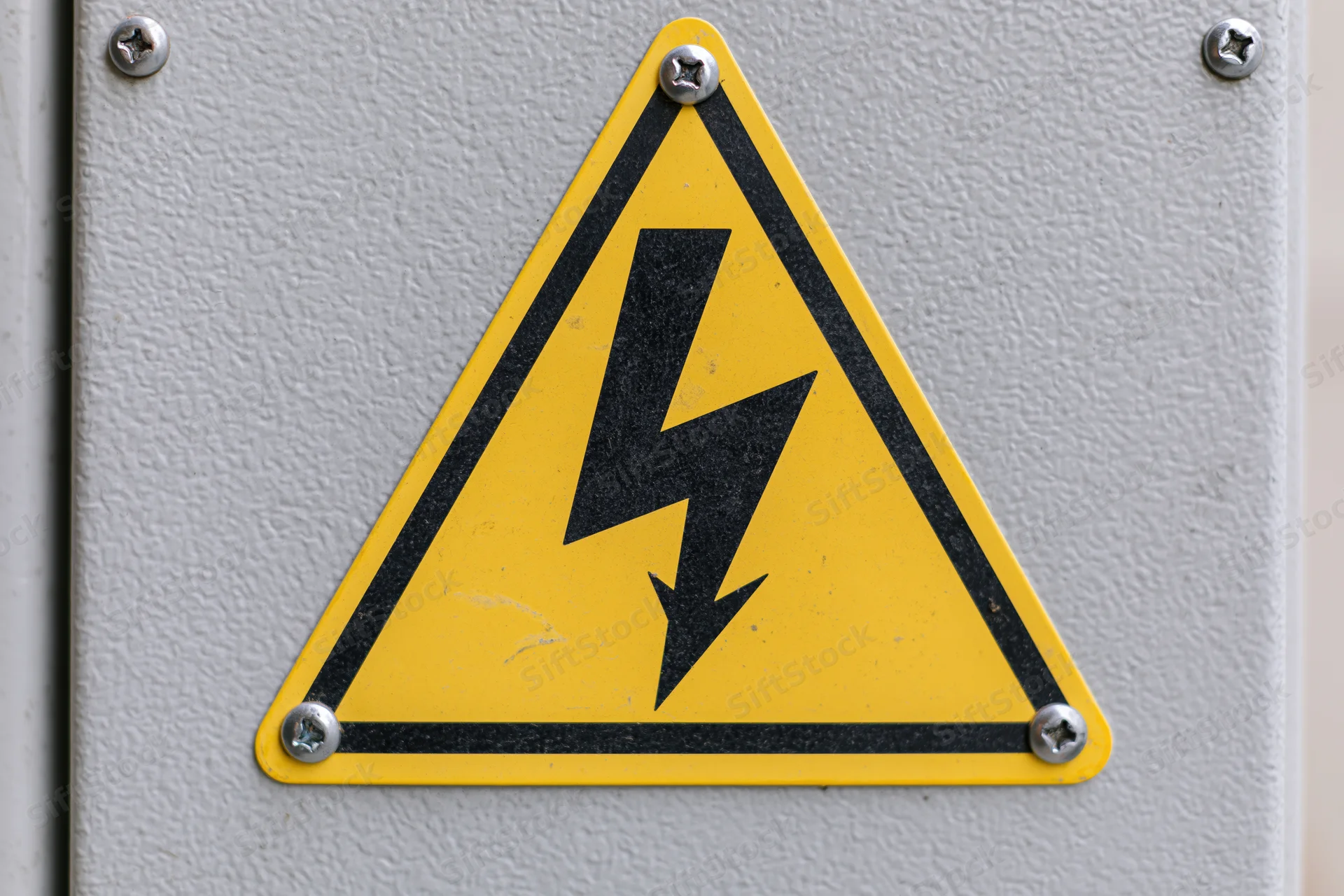 Yellow triangular warning sign with black lightning bolt symbol mounted on metal electrical panel