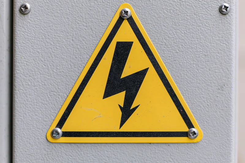 Yellow triangular warning sign with black lightning bolt symbol mounted on metal electrical panel