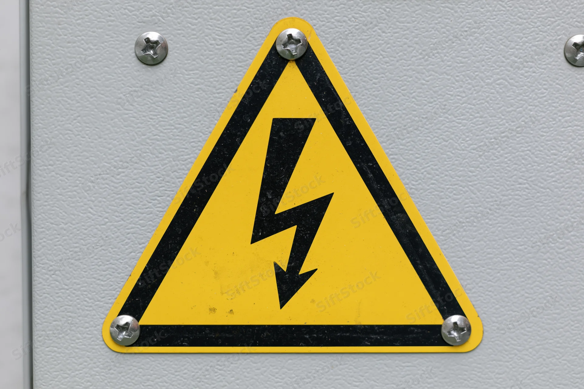 Yellow and black triangular warning sign with lightning bolt symbol on metal panel