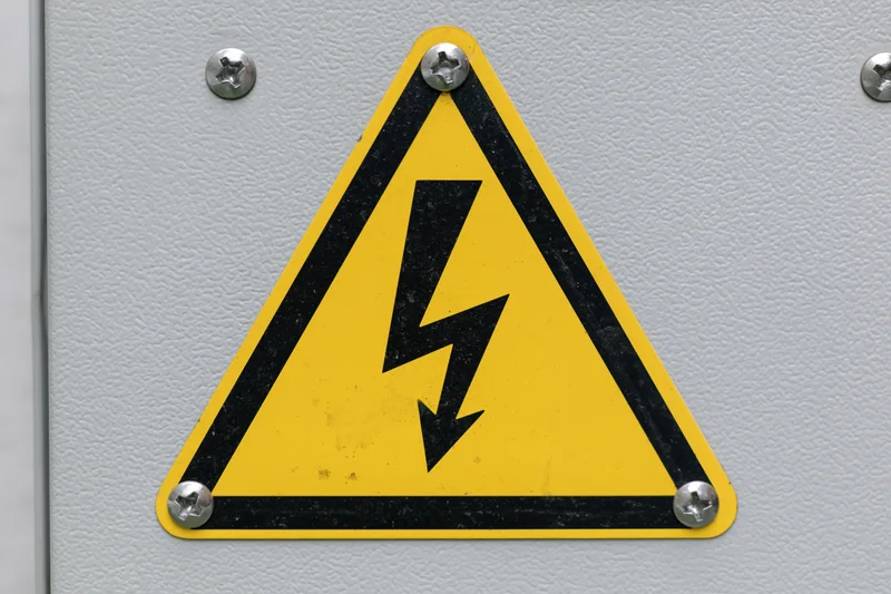 Yellow and black triangular warning sign with lightning bolt symbol on metal panel