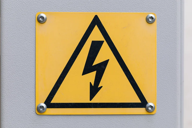 Yellow triangular high-voltage warning sign bolted to a gray metal panel