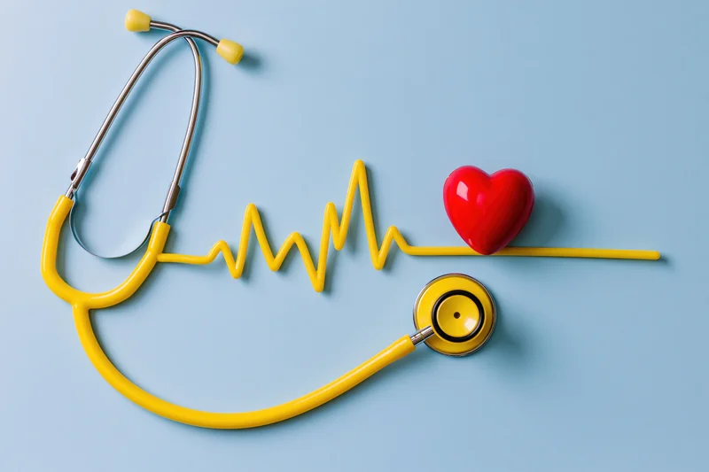 Yellow stethoscope with red heart and heartbeat line arranged flat on light blue surface
