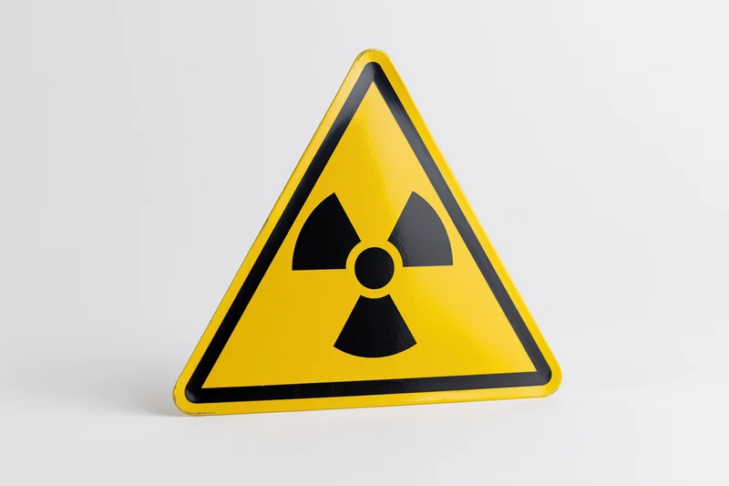 Yellow triangular radiation warning sign with black trefoil symbol on white background