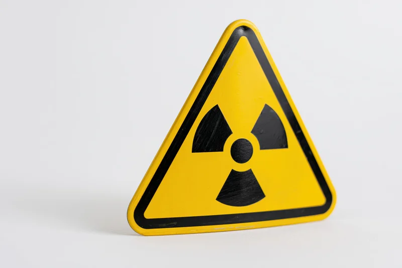 Yellow triangular radiation warning sign with black trefoil symbol on white background