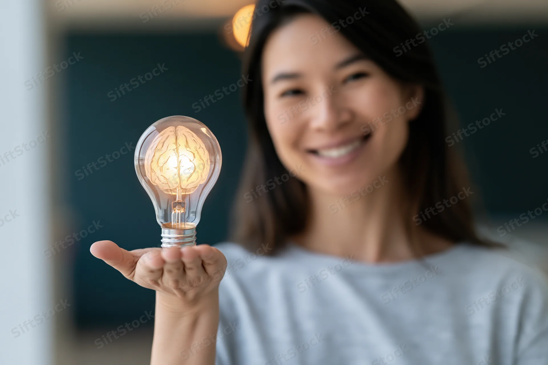 Smiling asian woman holding glowing glass lightbulb with brain filament in hand indoors