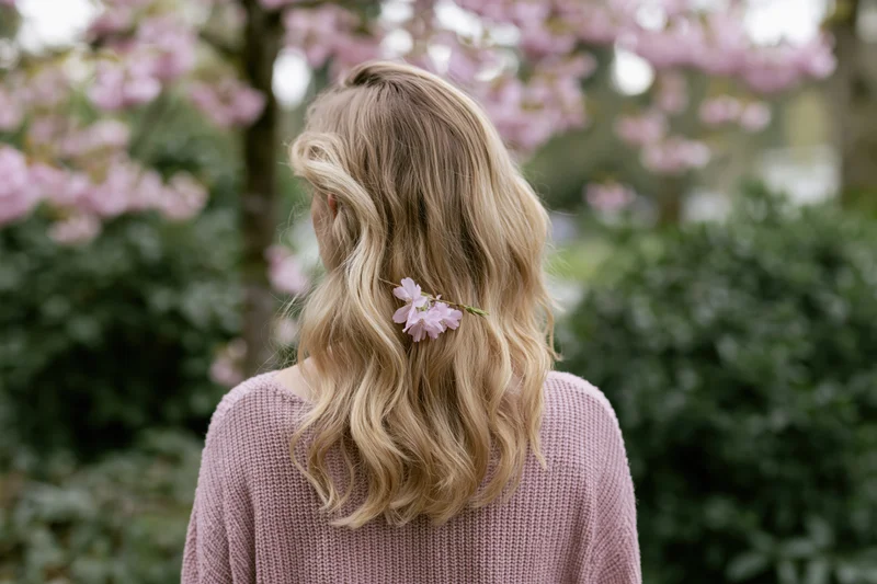 Woman with wavy blonde hair adorned with cherry blossoms standing in a garden