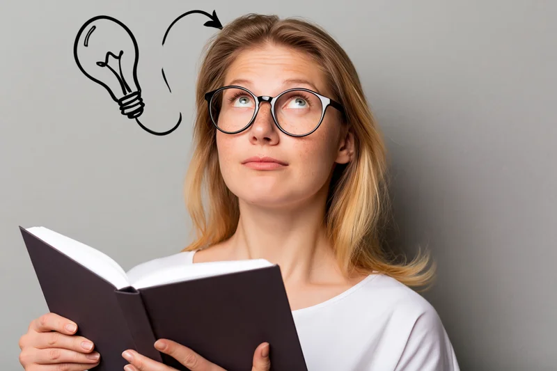 Young woman reading a book with a lightbulb symbol above her head indicating an idea