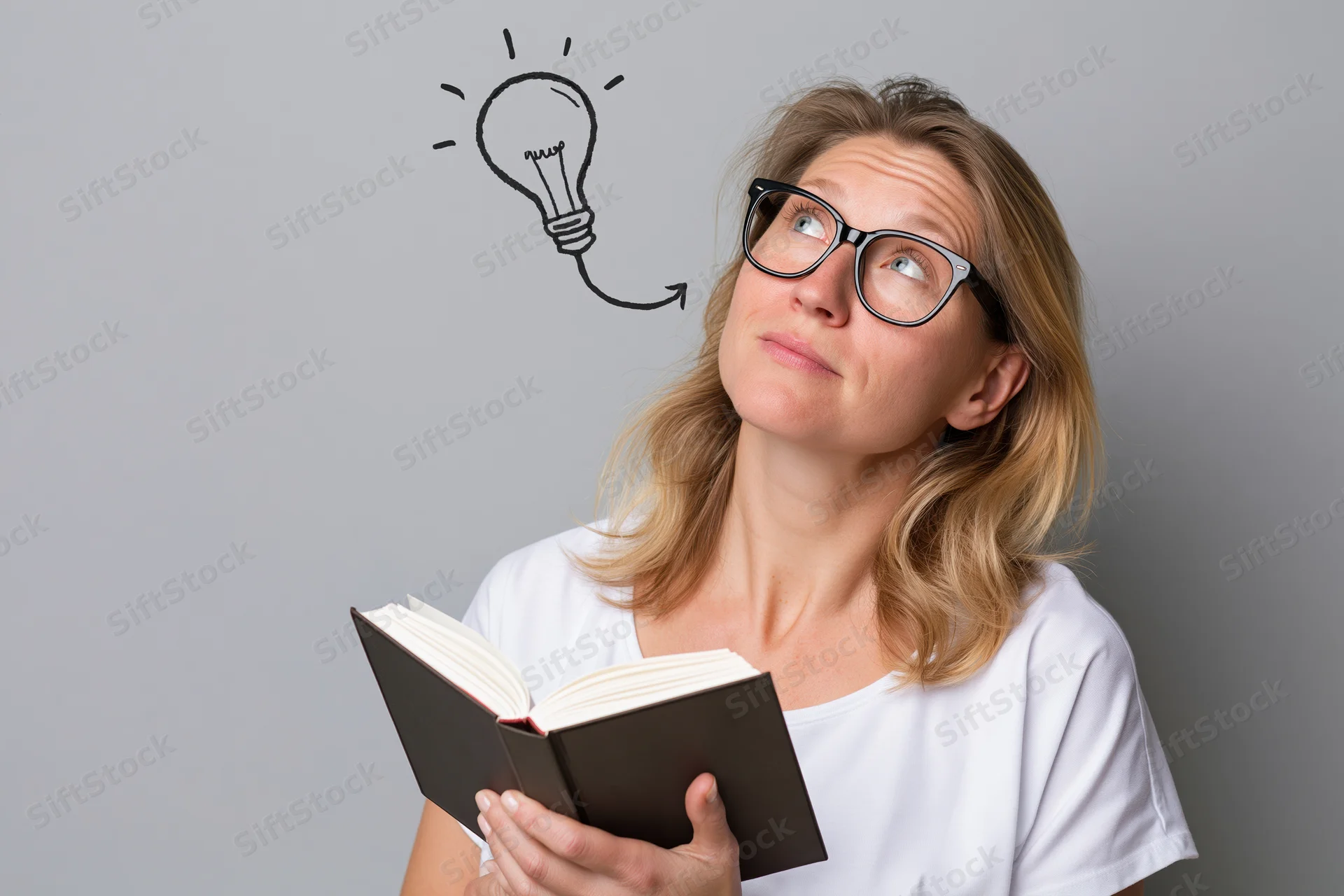 Woman holding open book looking upward with illustrated lightbulb above her head