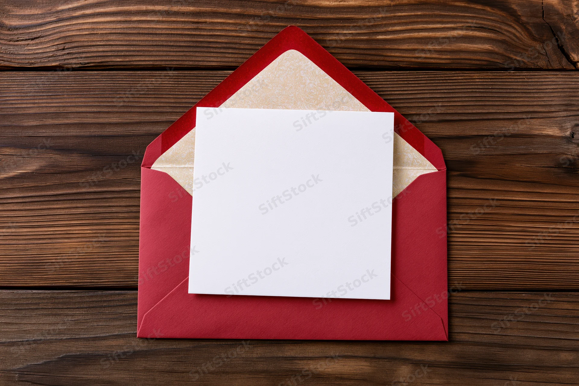Blank white square card resting on open red envelope on wooden surface
