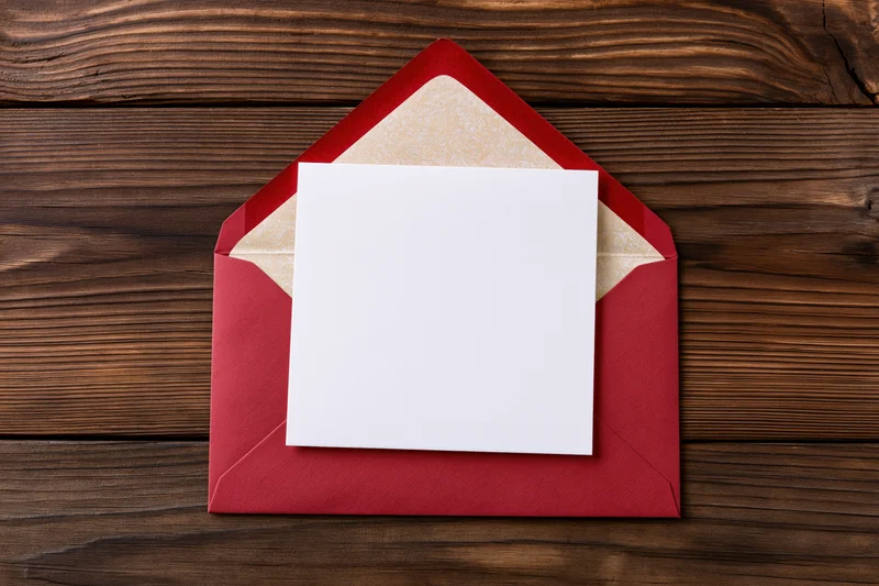 Blank white square card resting on open red envelope on wooden surface