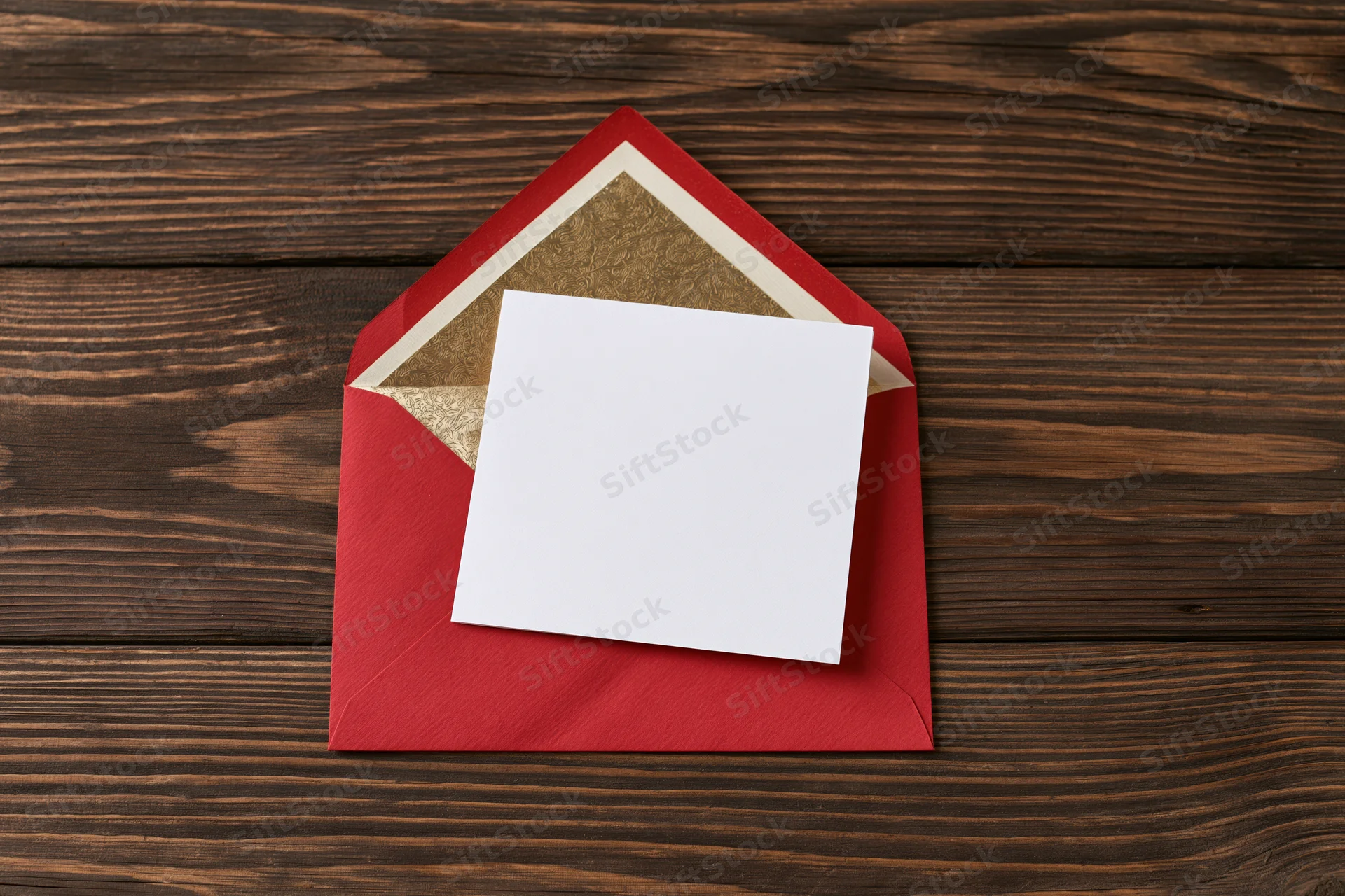 Blank white card resting on open red envelope on dark wooden surface