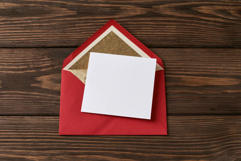 Blank white card resting on open red envelope on dark wooden surface
