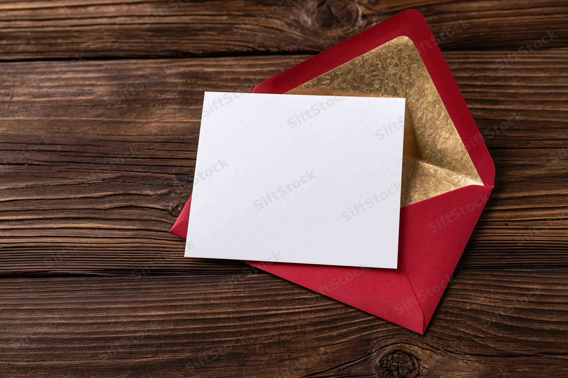 Blank white card resting on open red envelope with gold lining on dark wooden surface