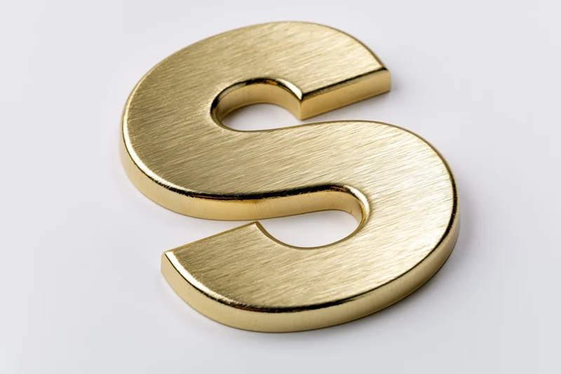 Golden three-dimensional letter s on a white surface