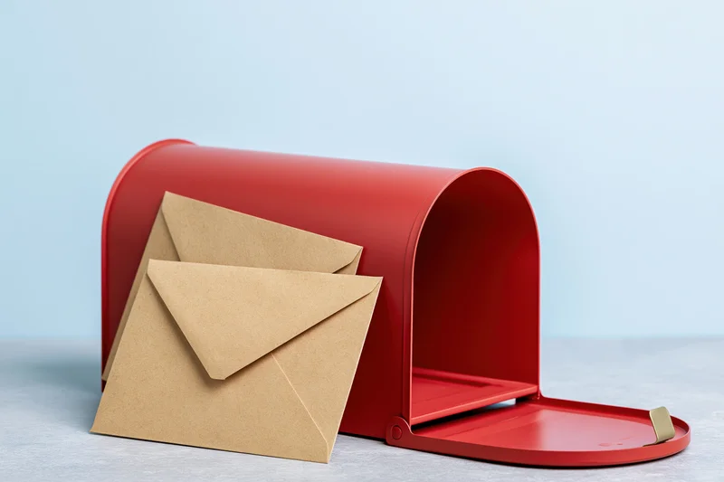 Red mailbox with open door and kraft envelopes on light surface