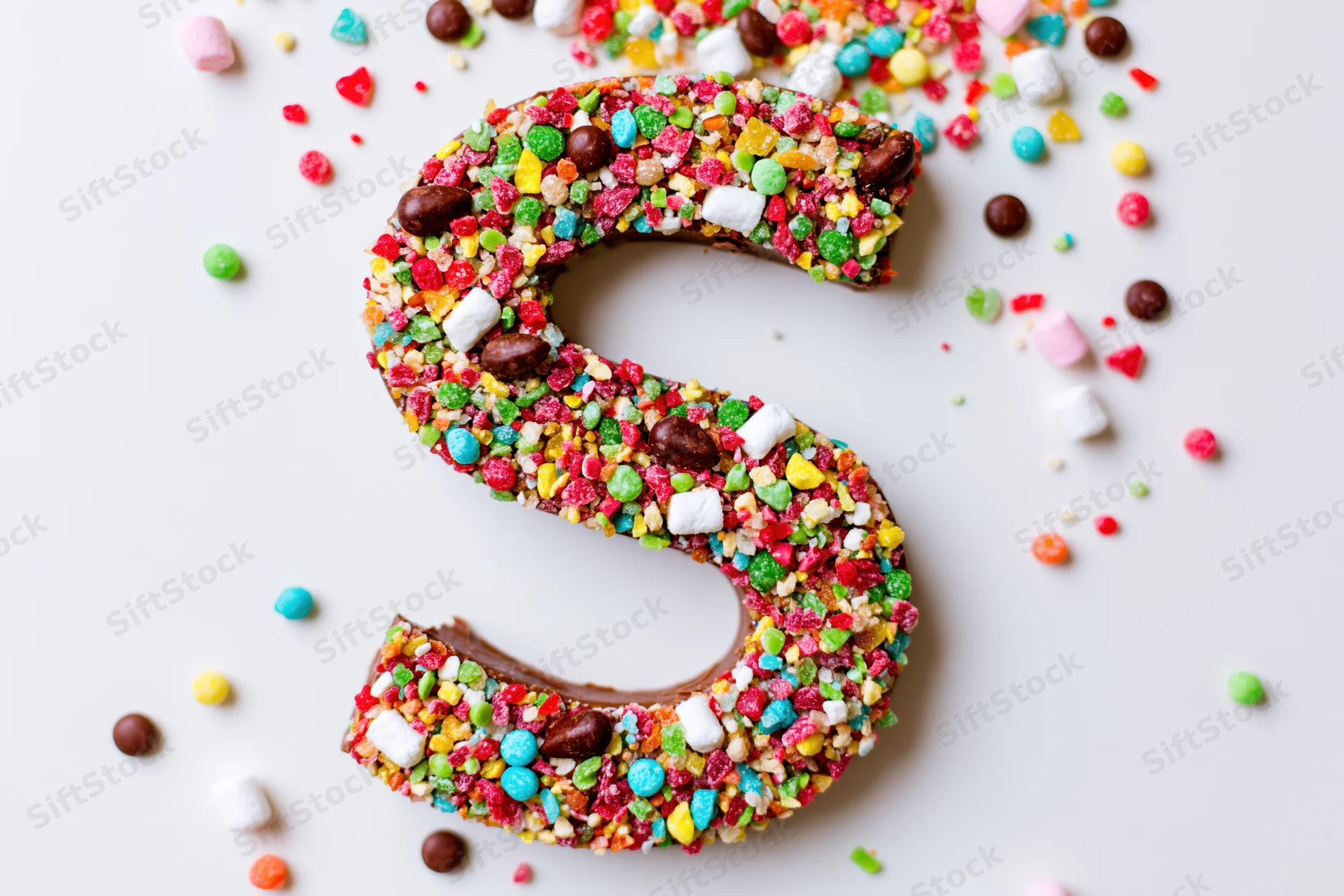 Chocolate letter s shaped dessert covered in colorful candies on white background