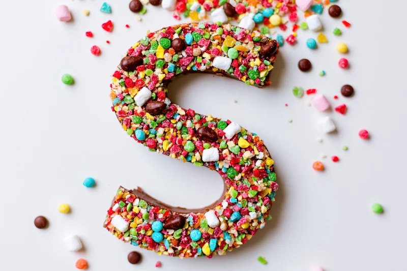 Chocolate letter s shaped dessert covered in colorful candies on white background