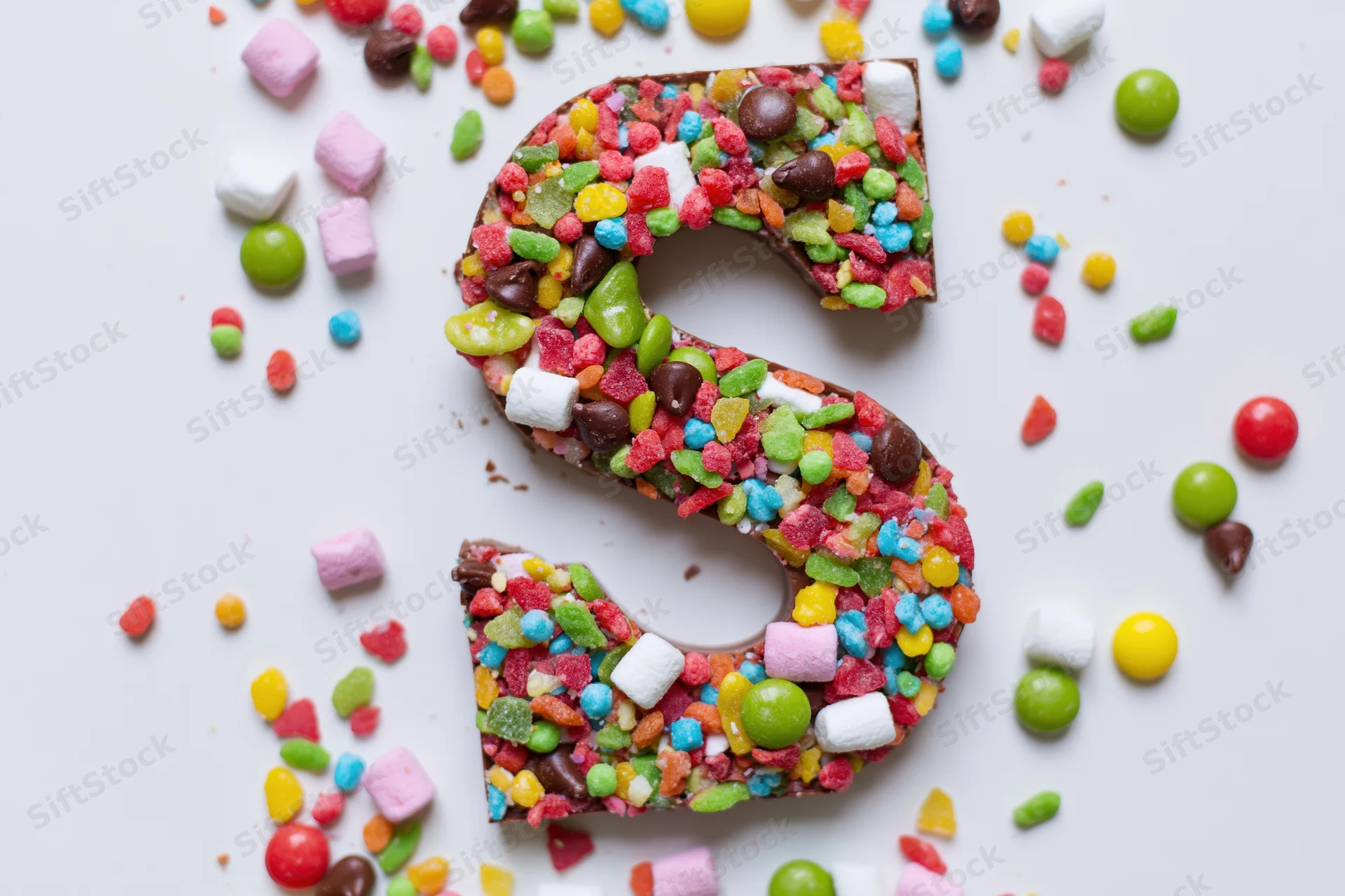 Chocolate letter s covered in colorful candies on white surface