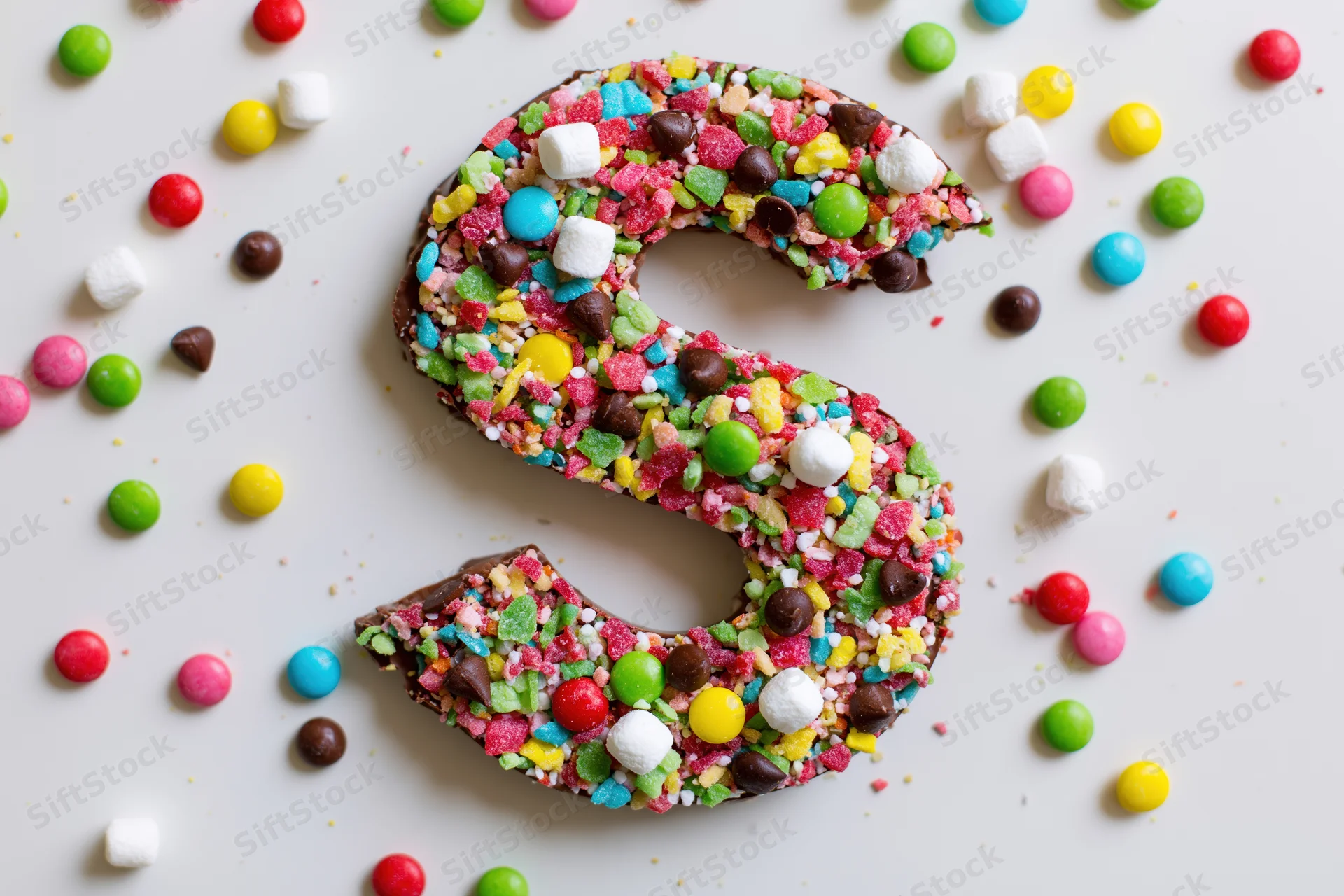 Chocolate letter s covered in colorful candies on white surface