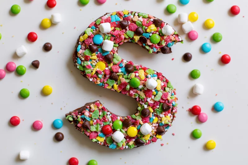 Chocolate letter s covered in colorful candies on white surface