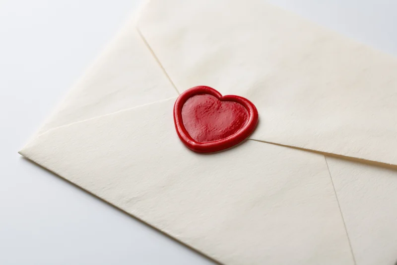 Cream paper envelope sealed with red wax heart on white background
