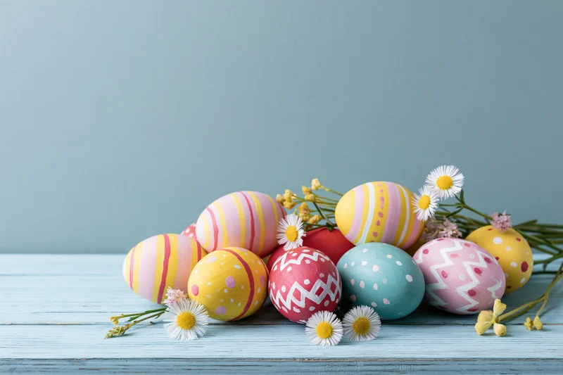 Hand-painted easter eggs with daisies arranged on a light blue wooden table