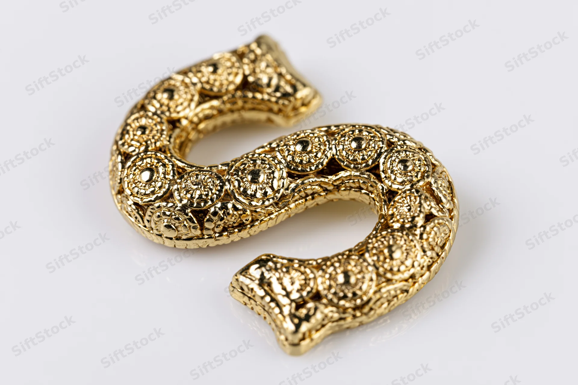 Polished gold decorative letter s with textured floral pattern on white background