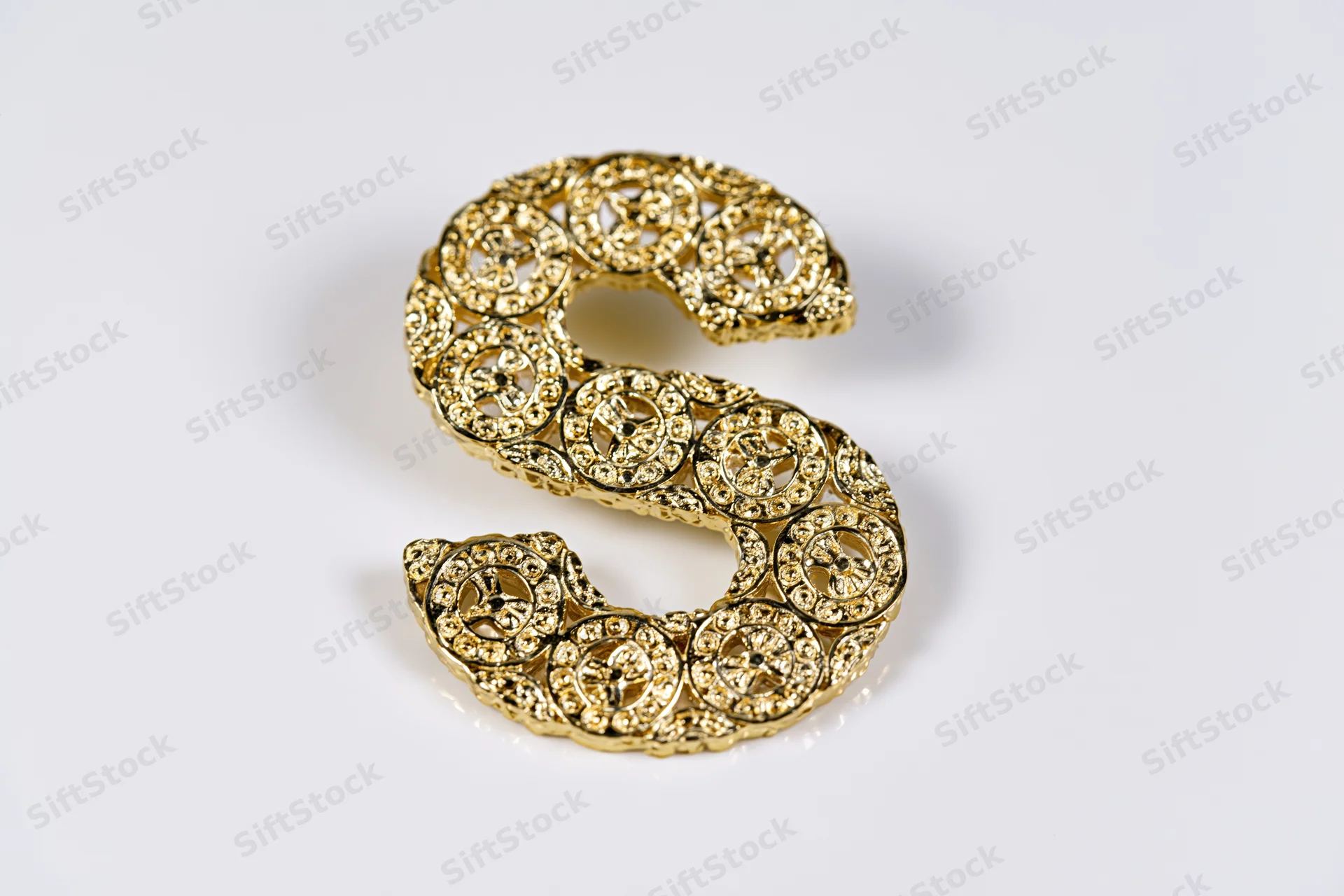 Polished gold decorative letter s with intricate filigree pattern on white background